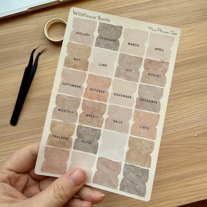 Könnte beinhalten: Ein Blatt mit Aquarell-Planer-Tabs im Wildflower Soirée-Stil. Die Tabs sind mit den Monaten des Jahres, den Wochentagen und anderen Planer-Kategorien wie "Tracker", "Notizen", "Listen", "Monatlich", "Wöchentlich" und "Täglich" beschriftet.
