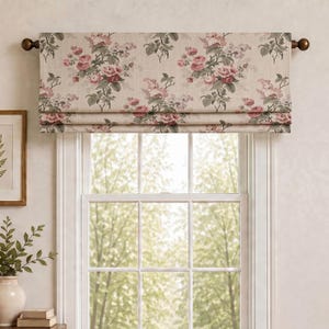 Op de afbeelding: Een stoffen raamvalance met een bloemenpatroon van roze rozen en groene bladeren op een lichtbeige achtergrond. De valance is gemonteerd op een donkerbruine gordijnroede met ronde knoppen, boven een wit raamkozijn.