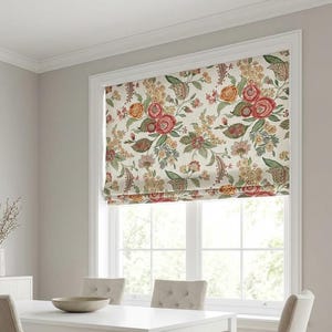 Puede incluir: Un comedor con una mesa blanca y cuatro sillas tapizadas beige. Una cortina romana con estampado floral cuelga de la ventana. La cortina tiene flores rojas, naranjas y verdes sobre un fondo crema.