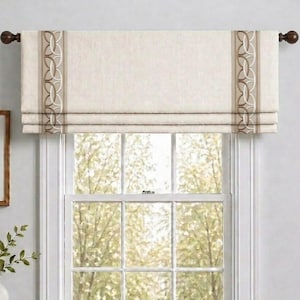 May include: A beige fabric window valance featuring a textured weave and two vertical bands of brown and white interlocking circular patterns. The valance is mounted on a dark brown curtain rod with round finials, positioned above a window.