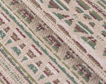 May include: Close-up of a beige fabric with a repeating pattern of green and burgundy geometric shapes. The fabric has a textured, woven look.