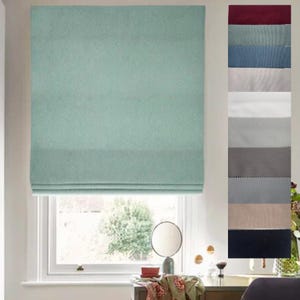 May include: A light blue roman shade window blind with a textured fabric. The blind is partially raised, revealing a window with a view of trees and a white wall. The blind is shown against a white wall.