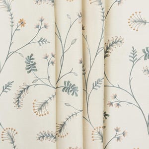 May include: Cream-colored fabric with a repeating floral pattern. The design features delicate gray stems with leaves and small, light orange and pink flower clusters. The fabric is folded, showing the texture and depth of the material.