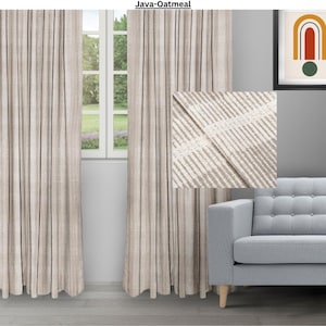 May include: A pair of beige curtains with thin black stripes. The curtains are made of a textured fabric and have a subtle sheen. The curtains are hanging in a window and are partially open. The curtains are in a living room setting with a couch and a picture on the wall.