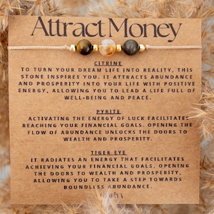 May include: A brown card with the text "Attract Money" in white lettering. The card features a bracelet with citrine, pyrite, and tiger's eye stones. The card describes the properties of each stone for attracting wealth and prosperity.