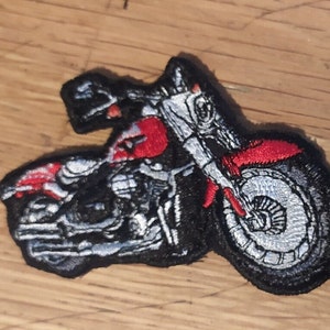 May include: An embroidered patch depicting a motorcycle in black and red. The motorcycle is detailed with silver stitching and has a red fuel tank.