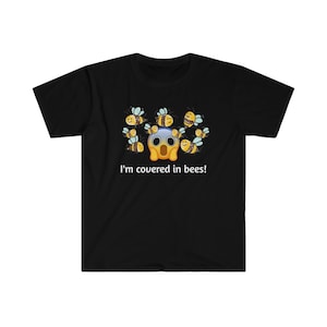 Puede incluir: Camiseta negra con un emoji angustiado rodeado de abejas de dibujos animados. El texto "I'm covered in bees!" está impreso debajo del gráfico. La camiseta es de un material suave.