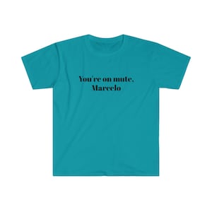 May include: A turquoise t-shirt featuring the black text "You're on mute, Marcelo". The crew neck tee is made of a soft material. The text is centrally placed on the front of the shirt, making a statement.