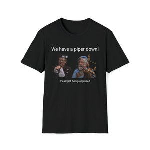 May include: Black t-shirt featuring a humorous graphic with two men and the text "We have a piper down!" and "It's alright, he's just pissed." The image shows a man in a kilt playing bagpipes.
