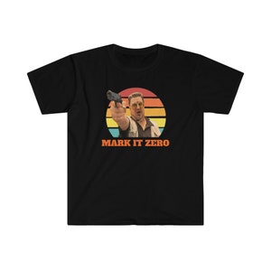 以下が含まれることがあります： 黒いTシャツ。男が銃を構えているグラフィックで、オレンジ、黄色、緑のストライプの夕焼け風の背景が特徴です。「MARK IT ZERO」の文字が下に印刷されています。