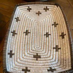 Op de afbeelding: Een rechthoekige geweven mand met een wit en bruin patroon. De mand heeft een donkerbruine rand en is gemaakt van natuurlijke materialen.