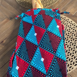 Könnte beinhalten: Eine rote, blaue und schwarze gemusterte Stofftasche mit Kordelzug. Die Tasche ist mit einem Laib Brot gefüllt.