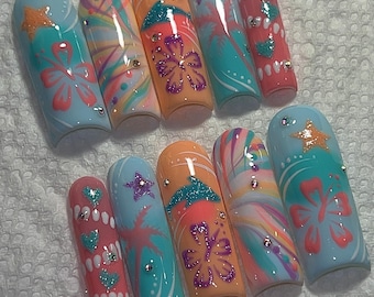 May include: A collection of ten long, almond-shaped artificial nails. Each nail showcases a unique design with pastel colours, glitter, and floral or tropical motifs. Some nails have star and heart accents.