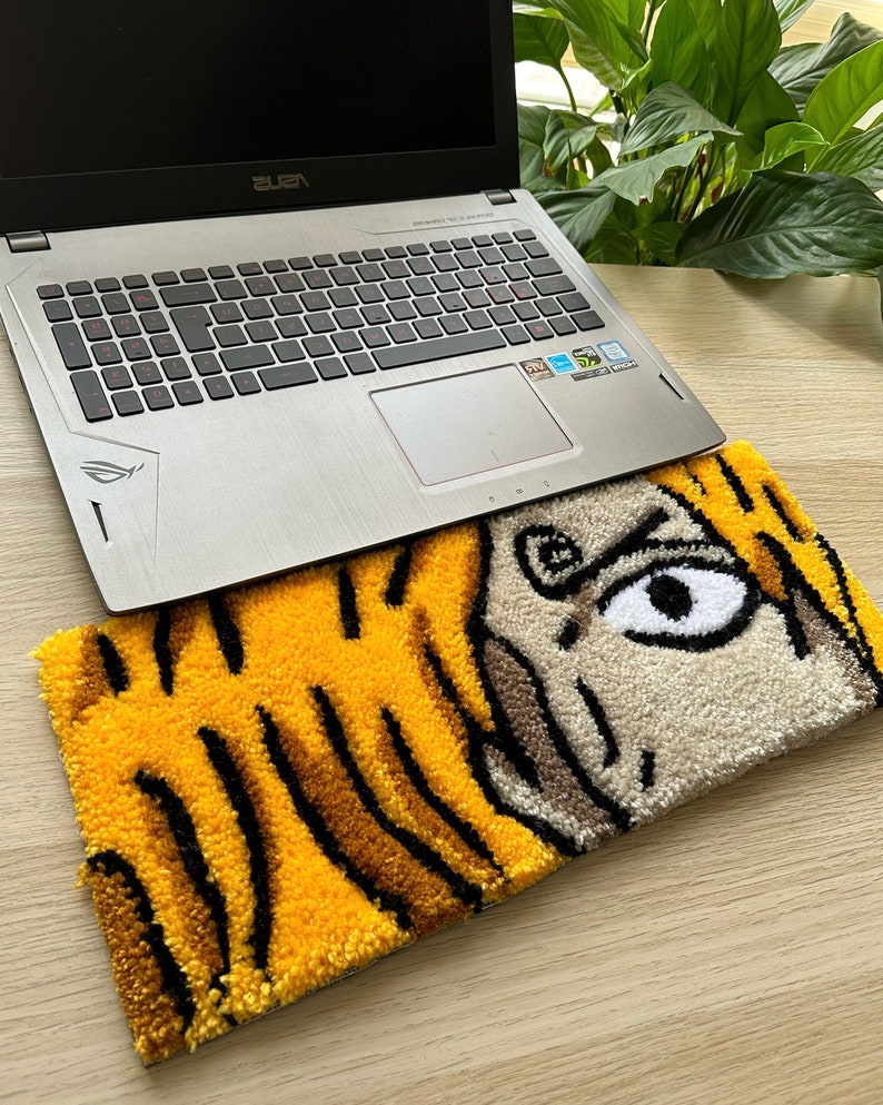 May include: A yellow and black rug with a cartoon character's face on it. The character has a large eye and blonde hair. The rug is on a wooden surface with a laptop computer on top of it.
