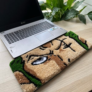 May include: A green, brown, and white rug with a cartoon face on it. The rug is on a wooden table with a laptop computer on top of it.