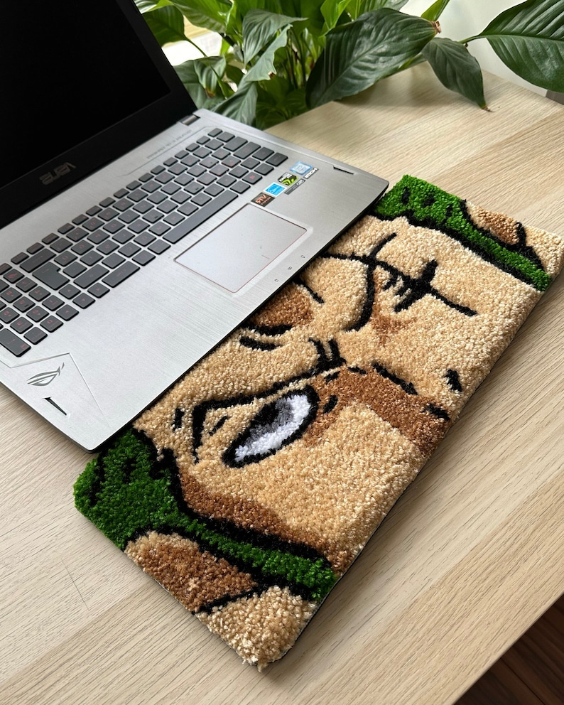 May include: A green and brown rug with a cartoon face on it. A silver laptop is sitting on top of the rug.