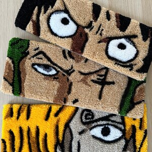 May include: Three hand-stitched wall hangings featuring cartoon characters with large eyes. The top hanging is brown and black with a white eye. The middle hanging is brown and green with a white eye. The bottom hanging is yellow and black with a white eye.