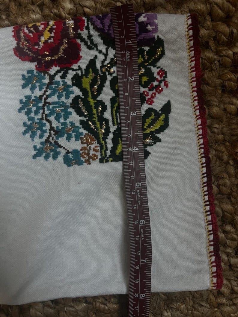 May include: White fabric with embroidered floral design in red, purple, blue, and gold. The edge is trimmed with red and gold stitching. A ruler shows the fabric is approximately 53 cm long.
