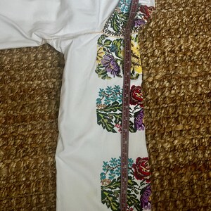May include: White embroidered sleeve with colourful floral patterns in red, purple, yellow, and blue. The sleeve is measured with a ruler, showing a length of approximately 50 cm. The embroidery is detailed and vibrant.