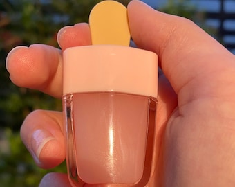 May include: A pink and clear popsicle-shaped lip gloss container with a yellow plastic top.