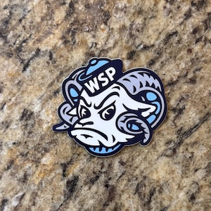 May include: A die-cut sticker featuring a stylized ram head mascot with a determined expression, wearing a small blue sailor hat. The design uses a color palette of white, dark navy blue, and light blue, with the letters WSP printed on the hat.