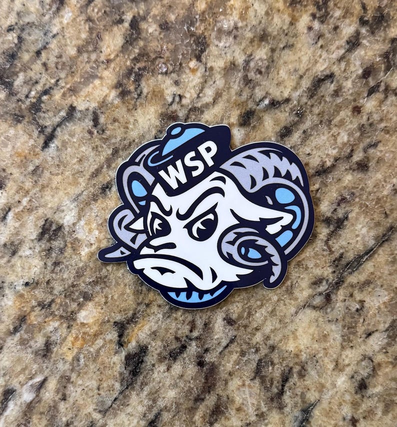 May include: A die-cut sticker featuring a stylized ram head mascot with a determined expression, wearing a small blue sailor hat. The design uses a color palette of white, dark navy blue, and light blue, with the letters WSP printed on the hat.