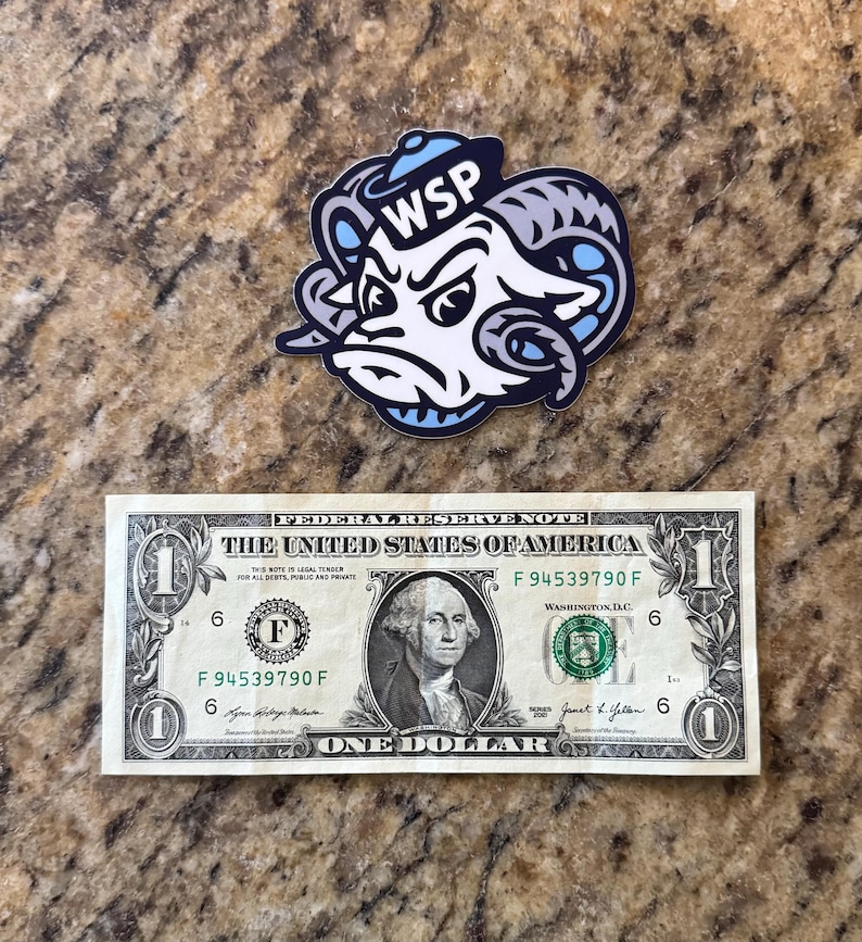 May include: A die-cut sticker featuring a stylized ram head mascot with large curved horns, wearing a small blue hat, and displaying the letters WSP in white. The sticker is positioned above a standard United States one-dollar bill for scale.
