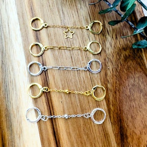 May include: Five gold and silver chain and hoop earrings with a star charm on one of the gold chains.