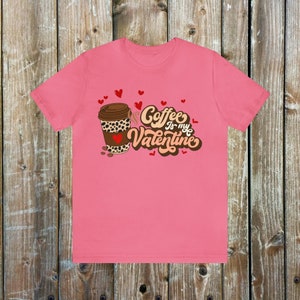 May include: Pink t-shirt with a brown coffee cup with a leopard print design and the text "Coffee is my Valentine" in brown and orange lettering with red hearts.