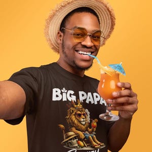 May include: A black t-shirt featuring a graphic of a lion wearing a crown and sunglasses, sitting in a chair with a cocktail. The text "BIG PAPA" is printed above the lion, and "Energy" is printed below. The lion is also holding a cocktail.
