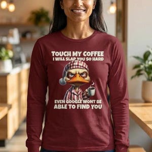Puede incluir: Camiseta burdeos de manga larga con el texto "TOUCH MY COFFEE I WILL SLAP YOU SO HARD EVEN GOOGLE WONT BE ABLE TO FIND YOU." La camiseta presenta un pato de dibujos animados con gorro de dormir y pijama, sosteniendo una taza de café.