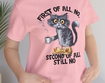 May include: Pink t-shirt featuring a grumpy cartoon cat holding a coffee cup and wearing duck slippers. The text on the shirt reads "FIRST OF ALL, NO. SECOND OF ALL STILL NO."