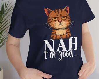 May include: Dark blue t-shirt with a cartoon cat illustration. The cat is brown and orange, with a grumpy expression. White text below the cat reads "NAH I'm good...". The t-shirt has a crew neck and short sleeves.