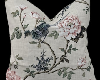 May include: A square throw pillow featuring a light beige linen-look fabric printed with a botanical pattern. The design includes a blue and grey bird perched on a brown branch, surrounded by large pink and white flowers and green leaves.