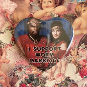 May include: A heart-shaped button with a picture of two characters from a fantasy movie. The text on the button reads "I support worm marriage".
