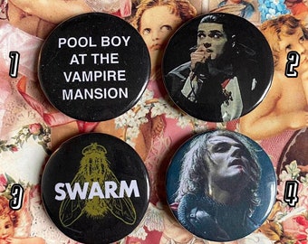 Puede incluir: Cuatro botones negros y blancos con diferentes diseños. El primer botón dice "Pool Boy at the Vampire Mansion". El segundo botón presenta una foto en blanco y negro de una persona con un micrófono. El tercer botón tiene una ilustración en blanco y negro de una mosca con la palabra "Swarm" impresa debajo. El cuarto botón presenta una foto en blanco y negro de una persona con el pelo largo.