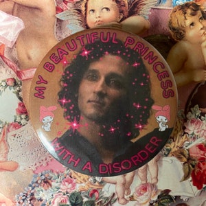 May include: A circular badge featuring a portrait of a person with long hair, framed by pink stars. The text "MY BEAUTIFUL PRINCESS WITH A DISORDER" is in pink. Two My Melody characters are on the badge.