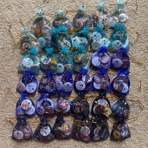 Puede incluir: Una colección de 36 botones pequeños, redondos y coloridos con varios diseños y textos. Los botones están empaquetados en bolsas individuales de malla azul y dorada. Los botones presentan imágenes de vampiros, corazones y el texto "Me encantan los vampiros".
