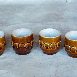 Peut inclure: Six tasses en céramique brun et blanc avec un motif circulaire. Les tasses sont disposées en rangée sur une surface gris clair.