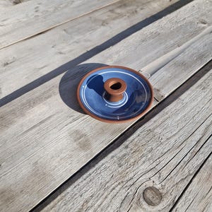 Può includere: Un porta incenso in ceramica fatto a mano. Il supporto presenta un interno blu scuro con un bordo bianco e marrone. Il centro ha un supporto cilindrico marrone per incenso. Posizionato su una superficie di legno invecchiato.