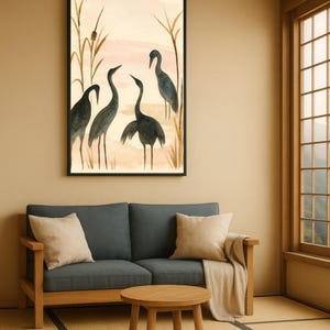 May include: A framed watercolor painting depicts four dark blue cranes in a marsh setting with tall reeds. The artwork hangs above a blue sofa with beige pillows and a wooden coffee table. The room has a neutral color palette.
