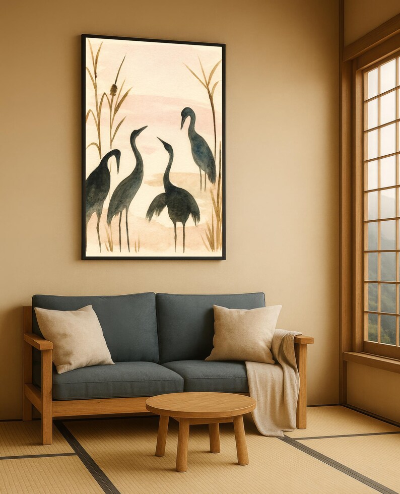 May include: A framed watercolor painting depicts four dark blue cranes in a marsh setting with tall reeds. The artwork hangs above a blue sofa with beige pillows and a wooden coffee table. The room has a neutral color palette.