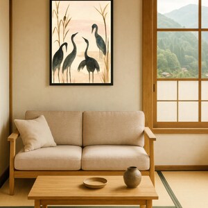 May include: A framed watercolor painting depicts four dark gray cranes in a marsh setting with tall reeds. The artwork hangs above a light beige sofa with a wooden coffee table and a small vase.