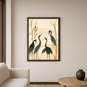 May include: A framed watercolor painting featuring five dark blue herons in a marsh setting. The artwork has a neutral color palette with beige, brown, and pink tones. The herons are depicted with long necks and legs, and the painting is framed in a dark brown frame.