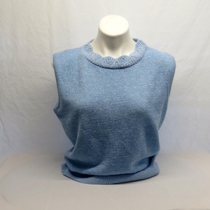 May include: A light blue sleeveless sweater displayed on a mannequin. The sweater has a scalloped neckline and a ribbed hem. The fabric appears to be a soft knit. The overall style is classic and versatile.