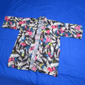 May include: A kimono-style robe with a vibrant tropical floral print. The robe features a black background with white, pink, blue, and yellow floral and palm leaf patterns. The robe is open-fronted with long sleeves.