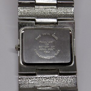 Może przedstawiać: Zbliżenie na tył stalowego zegarka. Na tylnej części zegarka widnieje napis "BASE METAL BEZEL", "FMDCT287 109 BATTERY 377 JAPAN MOVT RMD STAINLESS STEEL BACK". Pasek zegarka jest teksturowany.