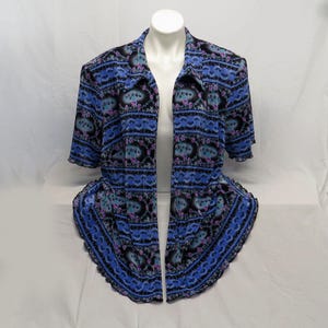 May include: A blue, black, and purple patterned open-front jacket with short sleeves. The jacket is displayed on a white mannequin. The pattern includes floral and geometric designs. The jacket has a ruffled hem.