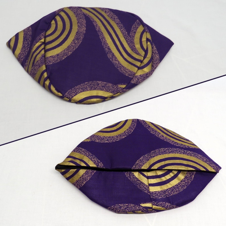 May include: A purple fabric pouch featuring a gold swirling pattern. The pouch is shown from two angles, displaying a rounded, folded shape with a dark interior lining visible at the opening of the bottom view of the accessory.