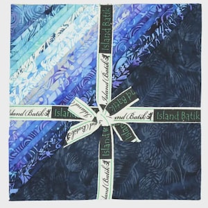 May include: A square stack of fabric squares tied with a white ribbon featuring the text Island Batik. The fabric pieces display a gradient of blue and purple shades, ranging from light cyan to deep navy, with various botanical and abstract patterns.